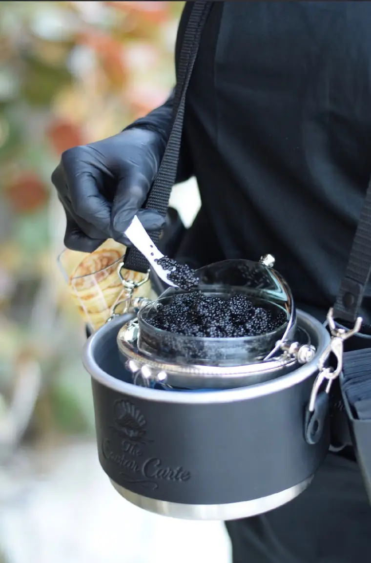 Caviar lifted from the embossed Caviar Carte tin by a gloved attendant