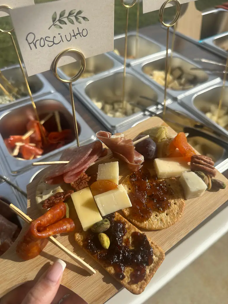 A guest board of prosciutto, salami, cheeses and fig jam, held up in front of the labelled prosciutto bin